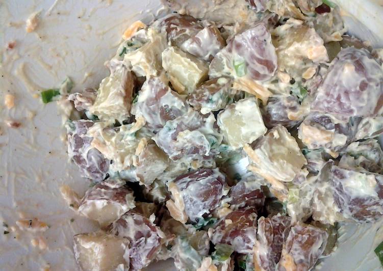 Close-up of creamy potato salad with chunks of red-skinned potatoes, herbs, and diced ingredients in a white bowl, warm beige and red tones.